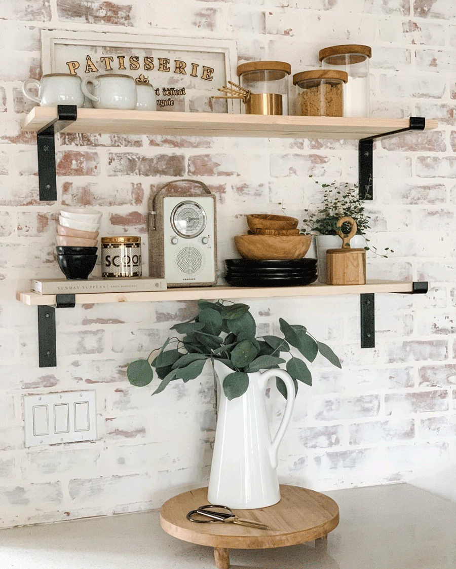 Exposed brick behind open shelving in kitchen.