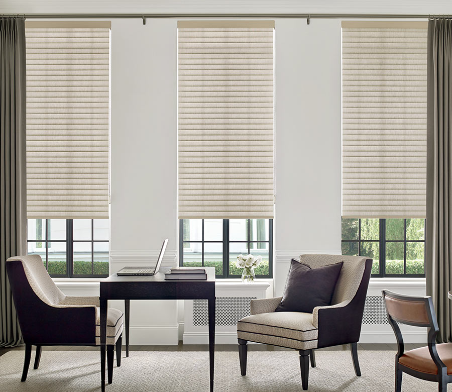 three windows in home office with black trim covered with cellular roller shades and draperies