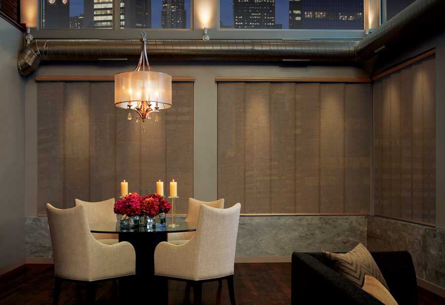 A smaller living room with Skyline gliding window panels, round table and four fabric chairs.