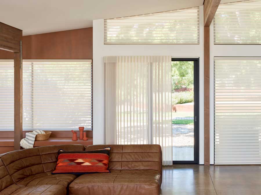 Living area with a dark leather couch, soft silhouette window coverings over a sliding door