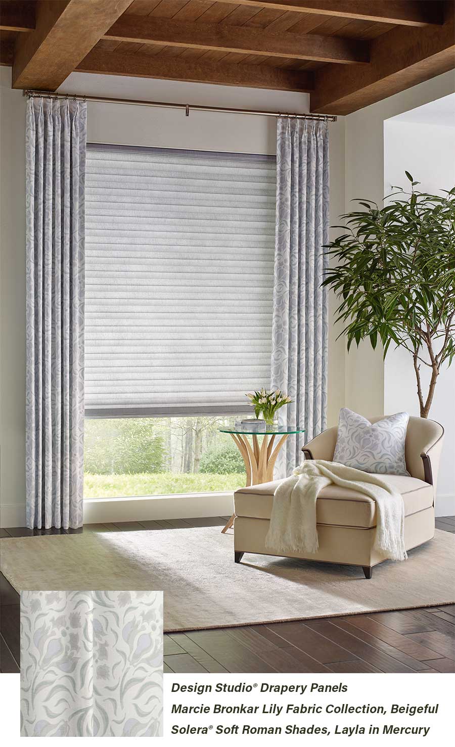 Neutral living room with soft designed draperies and roman shades over a long window next to a lounge chair in a living area