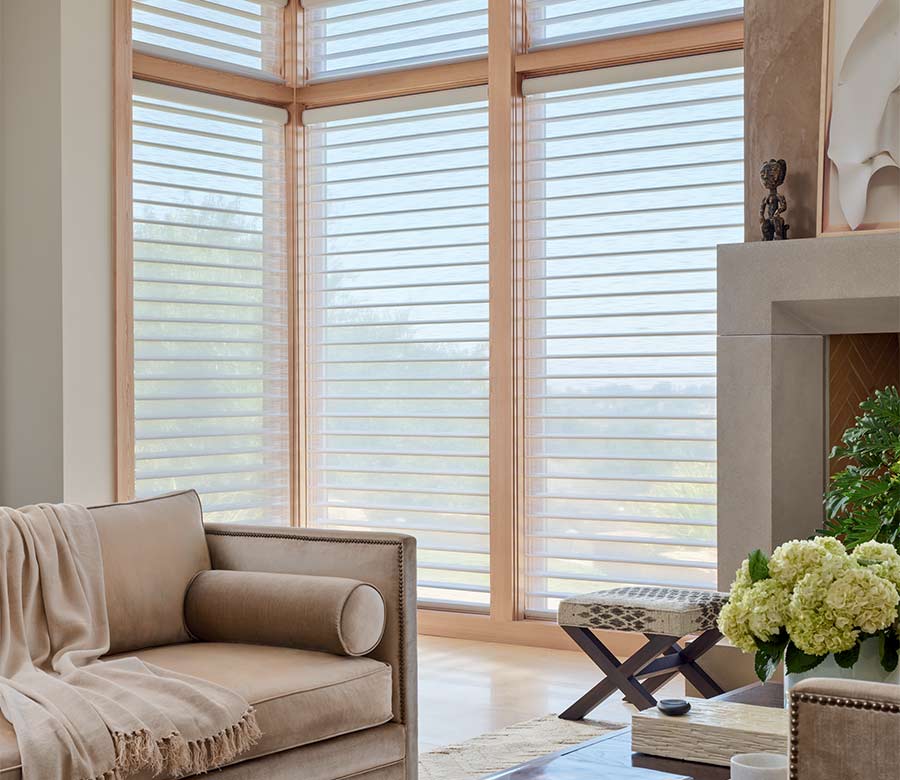 Silhouette® sheer window shades on floor-to-ceiling corner windows, diffusing natural light in a modern living room with sofa and fireplace