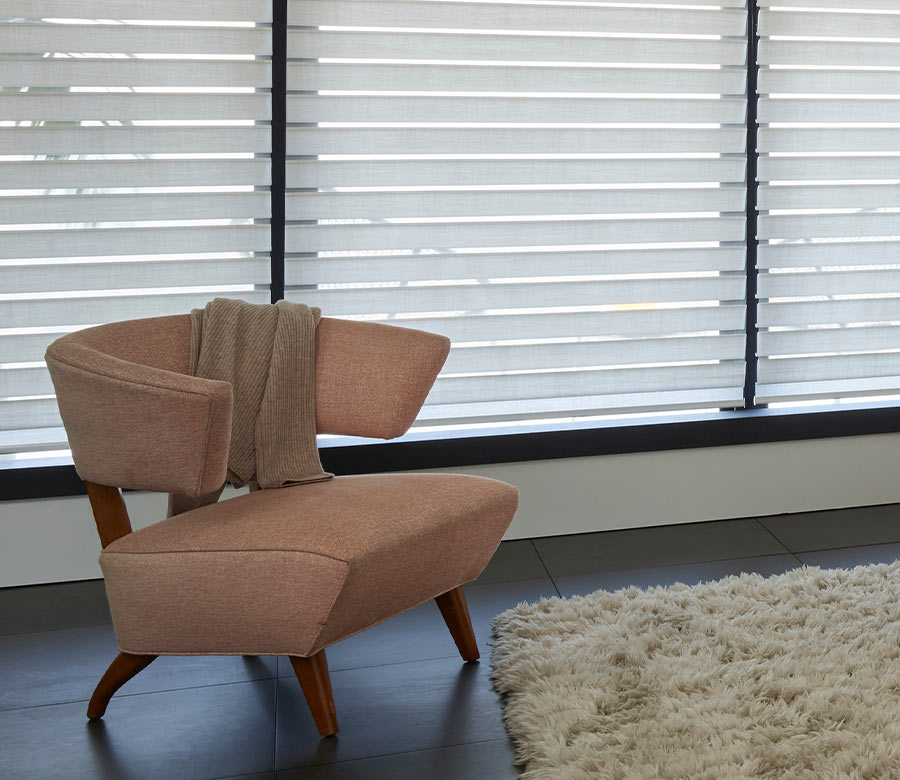 Silhouette® sheer window treatments behind a modern accent chair, softly filtering daylight through layered fabric vanes
